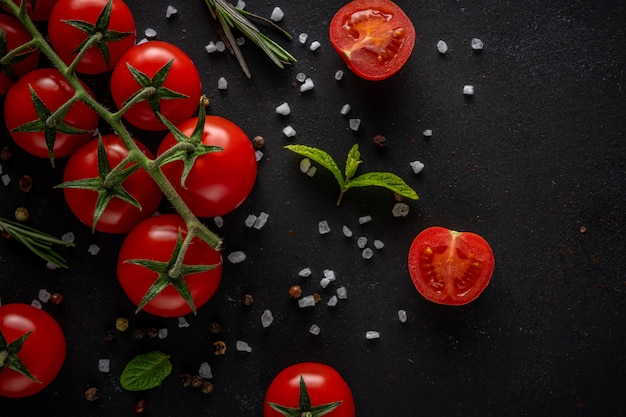 Tomates cerises fraîches sur fond noir avec des épices