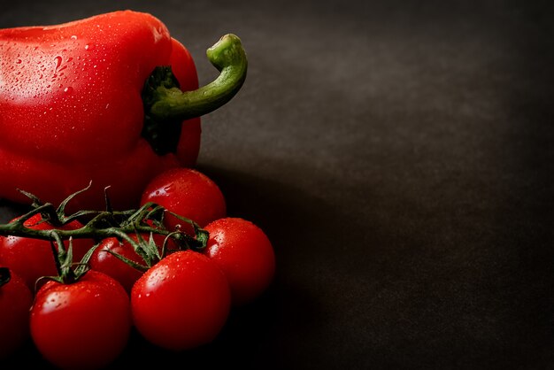 Tomates cerises fraîches mûres rouges sur branche et poivron sur surface sombre. Alimentation saine et régime