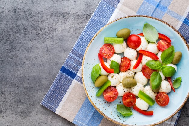 Tomates cerises, fromage mozzarella, basilic et épices sur tableau en ardoise grise. Ingrédients de la salade caprese traditionnelle italienne. Un plat méditerranéen.