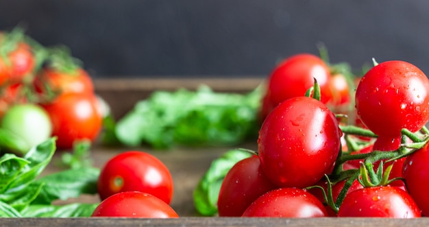 Tomates cerises mûres et basilic sur une surface en bois.