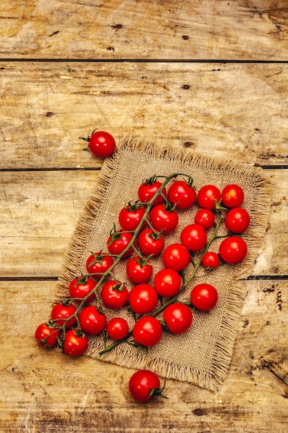 Tomates cerises mûres entières sur branche. Nouvelle récolte, sur un sac, fond de planches de bois, vue du dessus