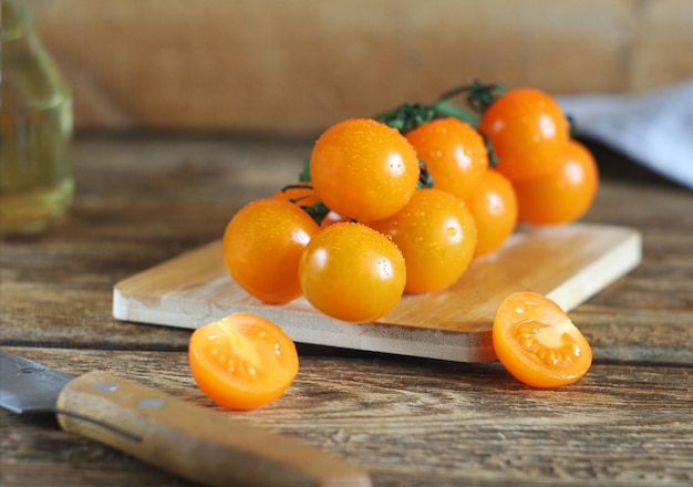 Tomates cerises orange lavées se trouvent sur une planche sur une table en bois à proximité se trouvent une serviette un couteau Derrière est l'huile