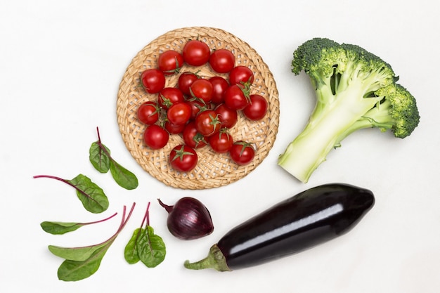 Tomates cerises en plaque en osier Brocoli d'aubergine et feuilles de blettes sur table