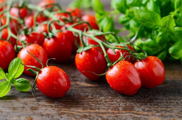 Photo tomates cerises rouges fraîches au basilic sur une table en bois rustique.