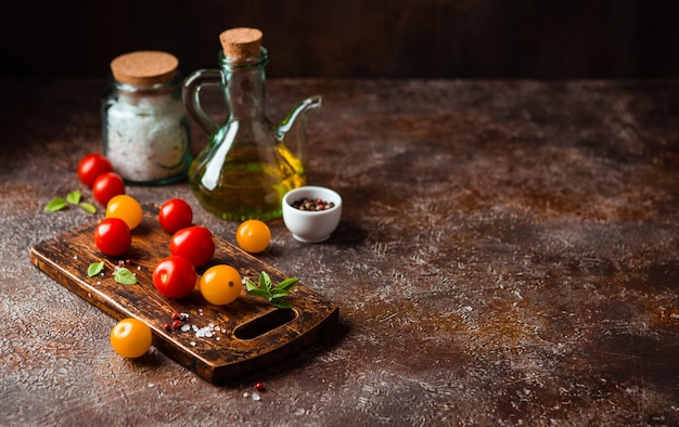 Tomates cerises rouges et jaunes, une bouteille d'huile d'olive, sel, poivre et basilic