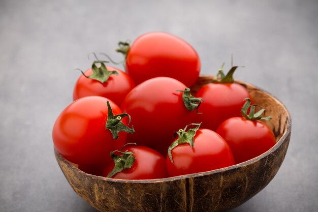 Tomates cerises. Trois tomates cerises dans un bol en bois sur fond gris.