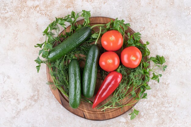 Tomates et concombre bio sur planche de bois avec des verts.