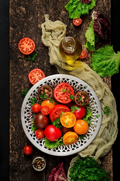 Tomates de différentes couleurs avec des herbes vertes dans un bol sur un tableau noir