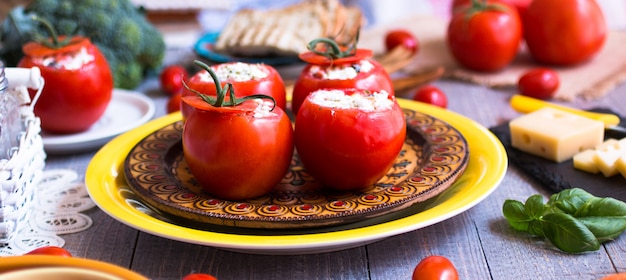 Tomates farcies au fromage et différents légumes sur une table en bois