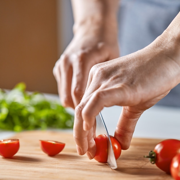 Tomates fraîches biologiques coupées au couteau les mains d'une fille sur une planche de bois. Cuisson pas à pas