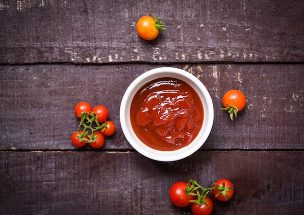 Tomates fraîches biologiques et ketchup dans une tasse de sauce tomate sur bois sombre - vue de dessus