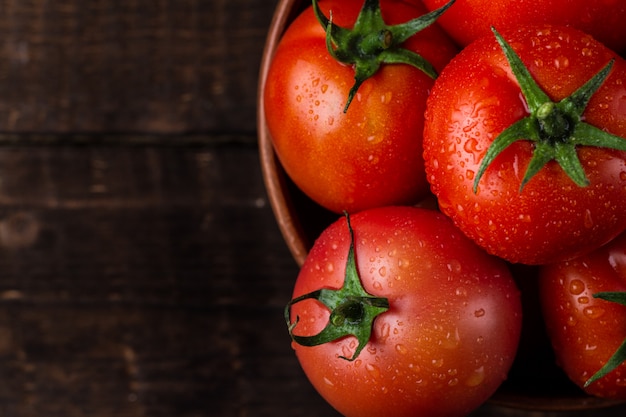 Des tomates fraîches dans une assiette sur un fond sombre se bouchent. Récolte de tomates. Vue de dessus