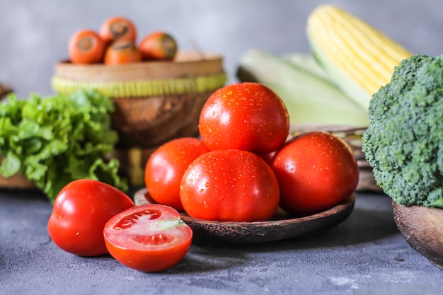 tomates fraîches dans un bol, autour des légumes, carotte, poivre noir, maïs, brocoli. Couper les tomates en tranches. Récolte des tomates.