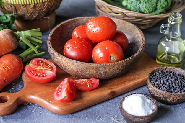 tomates fraîches dans un bol, autour des légumes, carotte, poivre noir, maïs, brocoli. Couper les tomates en tranches. Récolte des tomates.