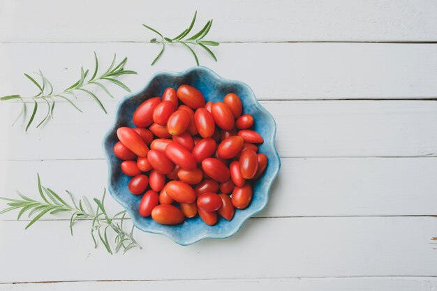 Tomates fraîches dans un bol bleu et romarin blanc. Vue de dessus.