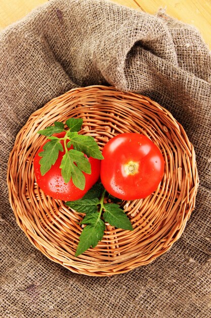 Tomates fraîches sur tapis en osier sur fond d'un sac