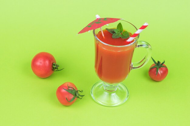 Tomates fraîches et un verre en verre avec du jus de tomate sur fond vert.