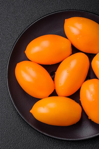 Tomates juteuses fraîches en forme de prune jaune sur un fond de béton à texture noire