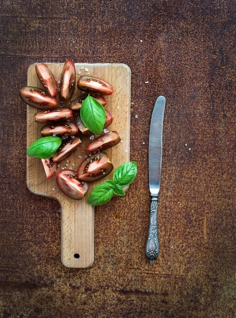 Tomates kumato mûres feuilles de basilic et couteau sur une planche à découper en bois rustique sur fond de métal rouillé grunge vue de dessus