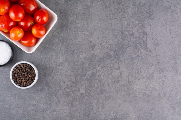 Tomates marinées avec des grains de poivre placés sur une table en pierre.