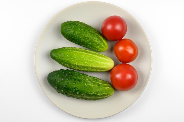 Tomates mûres et concombres sur une assiette sur fond blanc le concept de cuisson de légumes biologiques