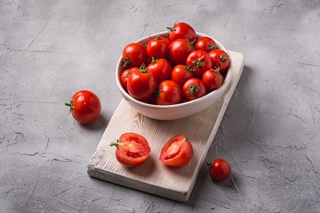 Tomates mûres fraîches entières et tranchées dans un bol et sur une vieille planche à découper en bois, table en béton en pierre, vue d'angle