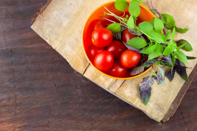 Tomates mûres fraîches, feuilles de basilic vert et violet dans un bol sur une planche à découper en bois