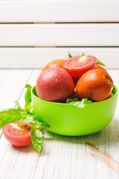 Tomates naturelles mûres et basilic dans un bol vert.