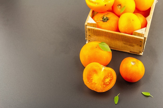 Tomates oranges mûres au basilic frais. Nouveaux légumes de récolte dans une caisse en bois. Fond de béton de pierre noire, espace de copie