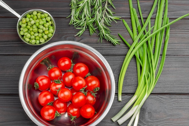 Tomates et petits pois frais dans des bols en métal Oignons verts et romarin Mise à plat Fond en bois foncé