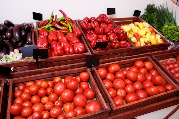 Tomates, poivrons, aubergines, choux, concombres et légumes verts dans des boîtes sur une étagère dans un magasin de légumes