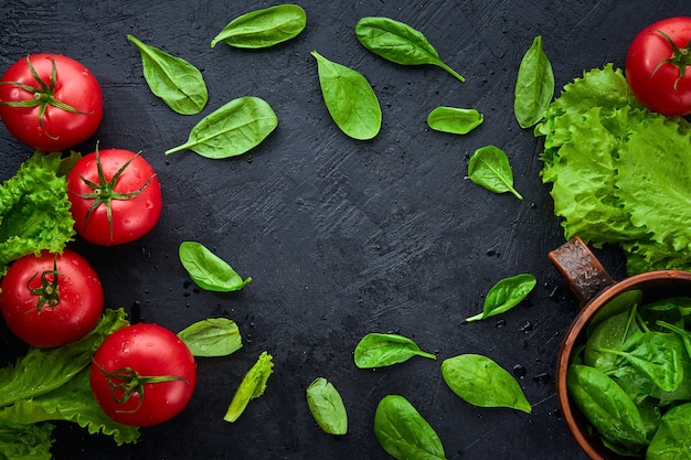 Tomates raisins fraîches avec des feuilles de salade sur fond noir. Herb, concept de cuisine de tomates rouges.