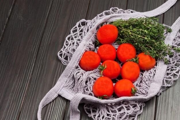 Tomates rouges et brindilles de thym dans un sac en filet naturel réutilisable. Concept zéro déchet. Fond en bois foncé. Mise à plat