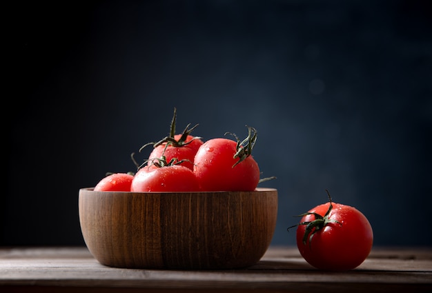 Tomates rouges fraîches dans un bol sur la vieille table en bois