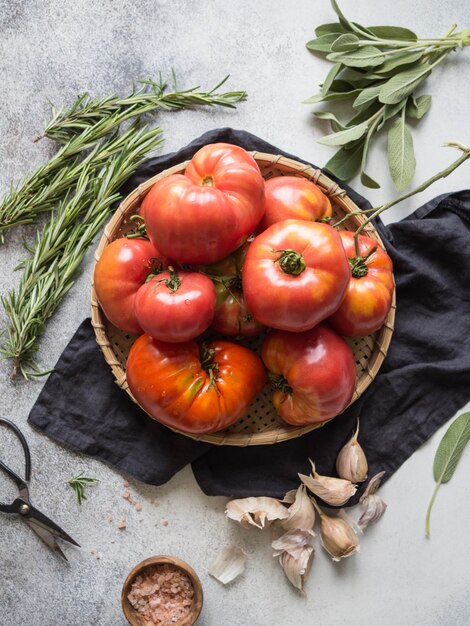 Tomates rouges fraîches sur un plat rond en osier, sel rose dans un bol en bois, ail.