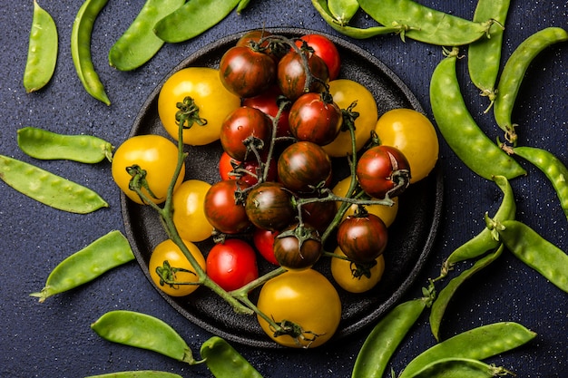 Tomates rouges et jaunes sur pate de fonte noire et pois vert sur fond noir