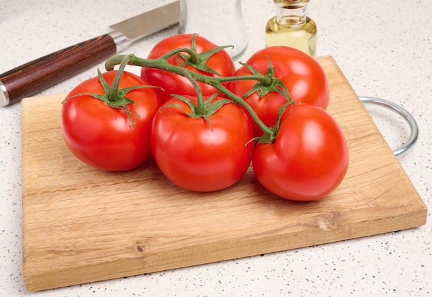 Des tomates rouges mûres sur une branche verte sur une table blanche, des légumes sains.