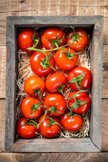 Tomates rouges mûres dans une boîte de marché en bois. Fond en bois. Vue de dessus.