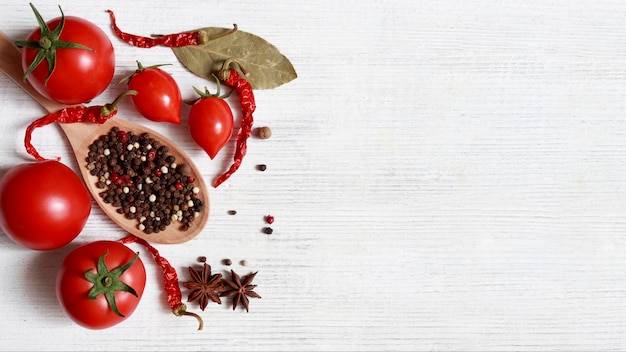 Tomates rouges mûres piments cardamome un mélange de poivrons sur une cuillère en bois sur un tableau blanc avec un espace réservé au texte Le concept de cuisson et de préservation des blancs