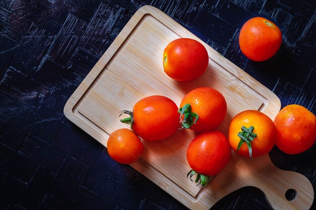 Photo tomates rouges sur une planche à découper en bois sur un fond noir.