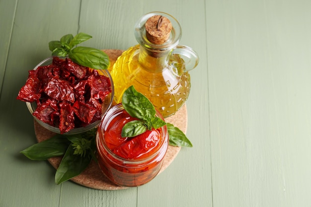 Tomates séchées au soleil dans un bocal en verre huile d'olive dans une bouteille en verre feuilles de basilic sur fond de bois de couleur