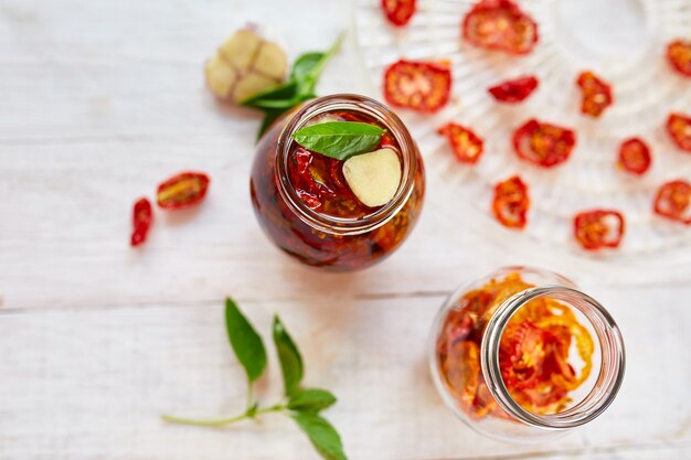 Tomates séchées au soleil maison aux herbes, ail à l'huile d'olive dans un bocal en verre sur fond de bois blanc. Vue de dessus. Imprimer pour la cuisine