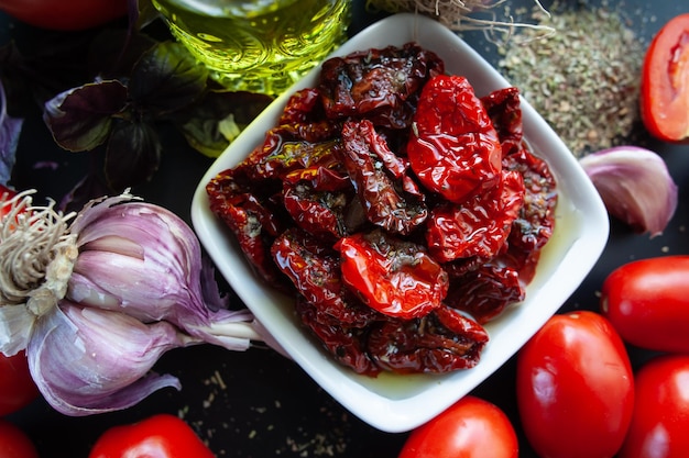 Des tomates séchées dans un bol entourées d'ingrédients, des épices, de l'ail et du basilic pour préparer une vue de haut de style rustique