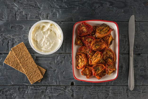 Tomates séchées avec du fromage à la crème et un couteau sur une table en bois. Apéritif de tomate méditerranéenne. La nourriture végétarienne. Mise à plat.