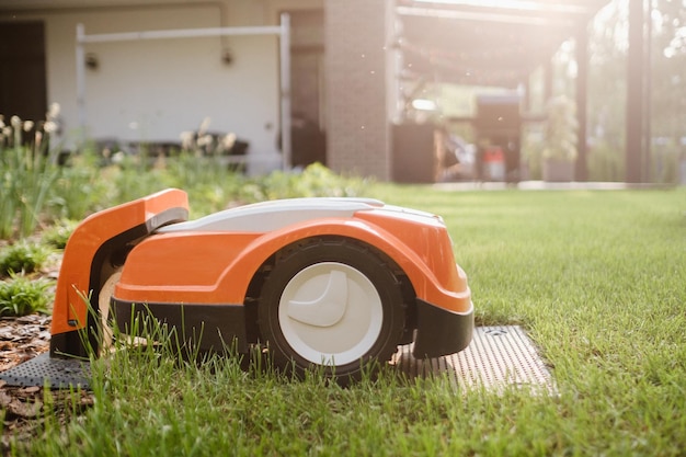 Une tondeuse à gazon robotique orange se tient sur la base et est chargée à partir de l'électricité dans la cour