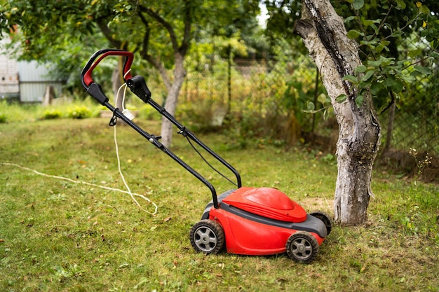 Tondeuse à gazon rouge en plein air dans l'arrière-cour herbe verte et arbres fruitiers fond Concept de jardinage