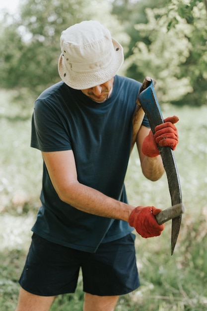 Tondre l'herbe de manière traditionnelle à l'ancienne avec une faux à la main sur une ferme de village domestique jeune agriculteur mature aiguisant la faux avec de l'herbe ou une pierre à aiguiser pour tondre les mauvaises herbes cultivées d'une terre agricole