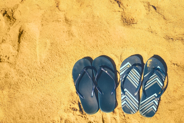 Tongs bleu marine sur fond de plage de sable jaune.