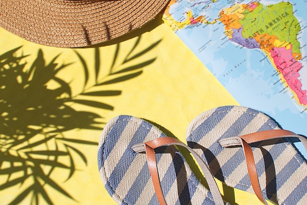 Tongs, carte du monde et chapeau de paille sur fond jaune