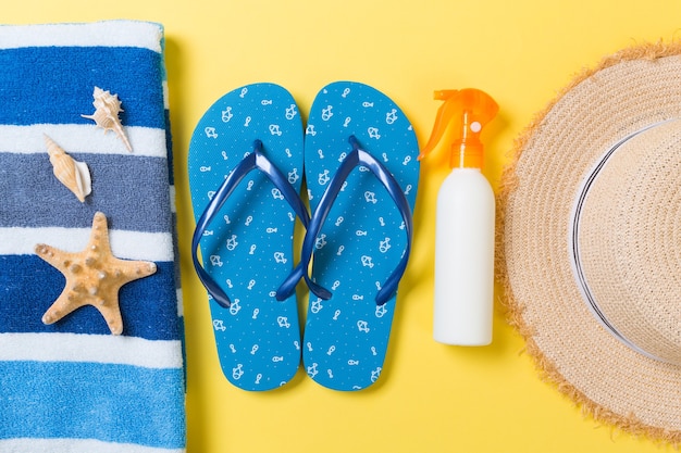 Tongs, chapeau de paille, étoile de mer, bouteille de crème solaire, spray de lotion pour le corps sur fond jaune vue de dessus. fond plat d'accessoires de mer plage d'été, concept de voyage.